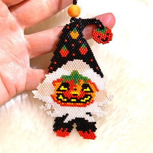 May include: A beaded Halloween gnome ornament with a black hat, orange and green pumpkin face, and red and orange pumpkin accents. The gnome is wearing black pants and red shoes.
