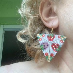May include: Triangle-shaped earrings with a white background and a pattern of red, green, and purple strawberries. The earrings are made of beads and have a gold-colored wire.