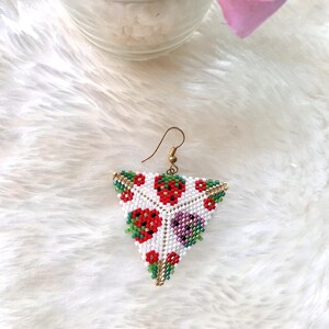 May include: Triangle-shaped beaded earrings with a white background and a pattern of red, green, and purple beads. The earrings are made with small beads and have a gold-colored wire.