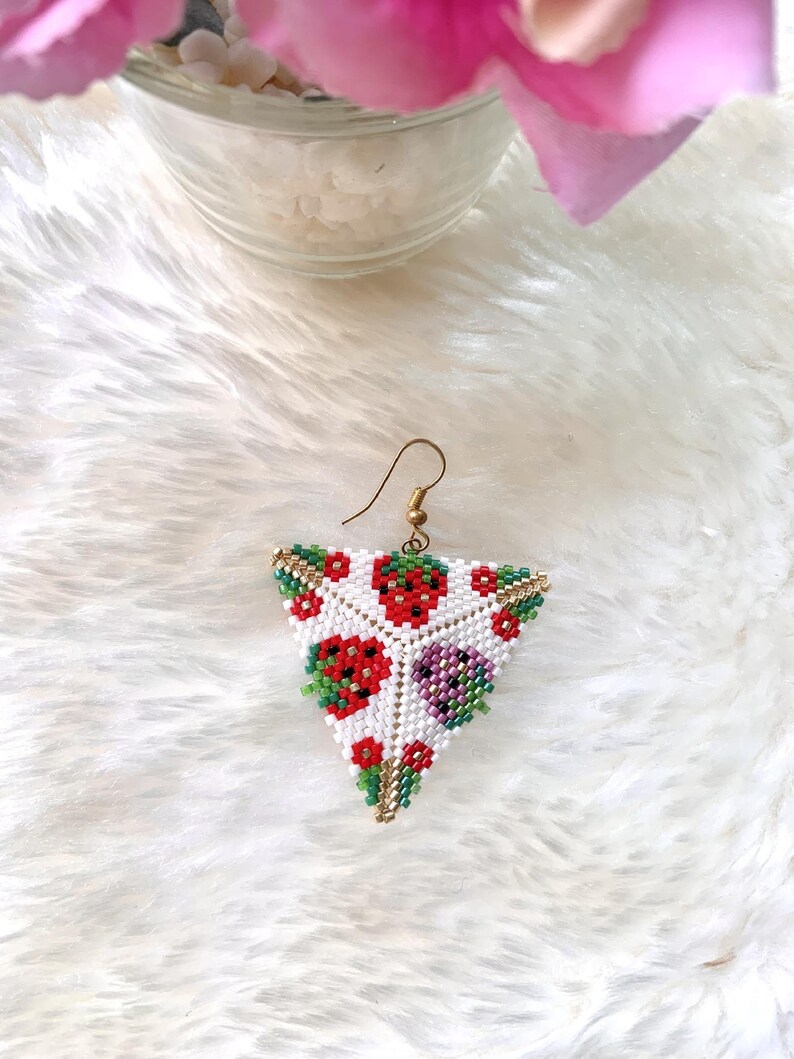 May include: Triangle-shaped beaded earrings with a white background and a pattern of red, green, and purple beads. The earrings are made with small beads and have a gold-colored wire.