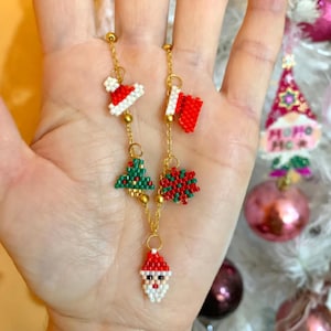 May include: A gold chain necklace with Christmas-themed charms. The charms are red, green, and white and feature Santa, a Christmas tree, and a Santa hat.
