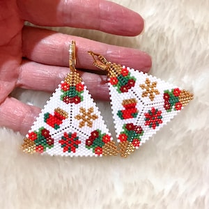 May include: Triangular Christmas earrings with white, red, green, and gold beadwork. The earrings feature festive designs including Christmas stockings, snowflakes, and floral patterns. The earrings are held by a hand.