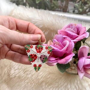 May include: Triangle-shaped beaded earrings with a white background and red, green, and gold floral designs.