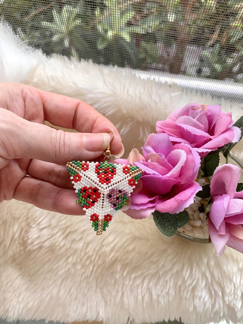 May include: Triangle-shaped beaded earrings with a white background and red, green, and gold floral designs.