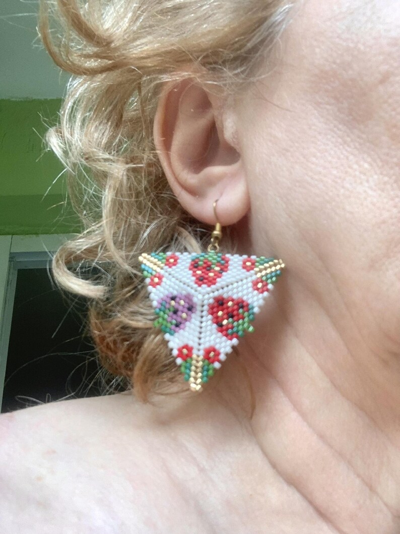 May include: Triangle-shaped beaded earrings with a white background and a pattern of red, green, and purple strawberries. The earrings are made with small beads and have a gold-colored wire.