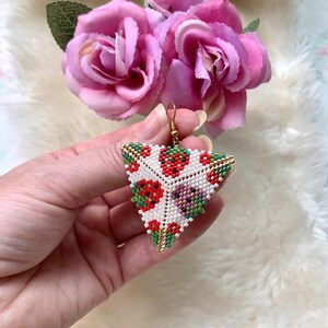May include: Triangle-shaped beaded earrings with a white background and a colorful pattern of red, green, and gold beads. The pattern resembles strawberries.