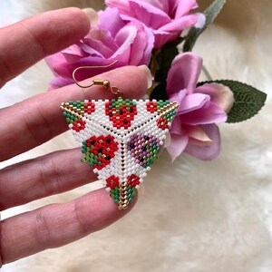 May include: Triangle-shaped beaded earrings with a white background and a pattern of red, green, and purple flowers. The earrings have a gold-colored wire loop for hanging.
