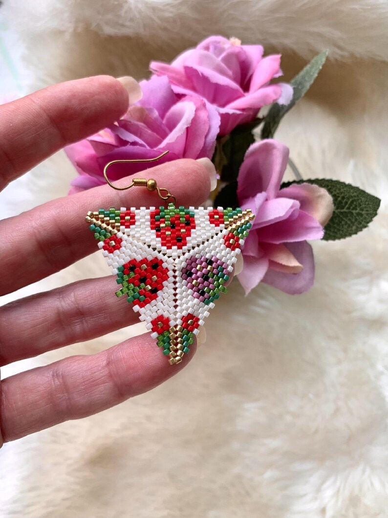 May include: Triangle-shaped beaded earrings with a white background and a pattern of red, green, and purple flowers. The earrings have a gold-colored wire loop for hanging.