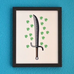 May include: A framed print of a black sword with a brown handle surrounded by green leaves.