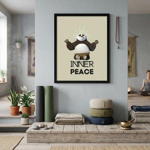 K&ouml;nnte beinhalten: Ein gerahmter Druck mit schwarzem Rahmen, der einen Cartoon-Panda in einer Yoga-Pose mit den Worten "INNER PEACE" zeigt. Das Bild wird in einem Yoga-Studio-Setting mit Yogamatten, Kissen und Pflanzen angezeigt.