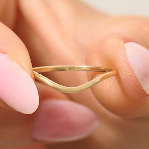 Op de afbeelding: Een delicate, goudkleurige chevronring. De ring heeft een gladde, gepolijste afwerking en een eenvoudig, minimalistisch ontwerp. De ring wordt tussen twee vingers gehouden, wat de elegante vorm en subtiele glans benadrukt.