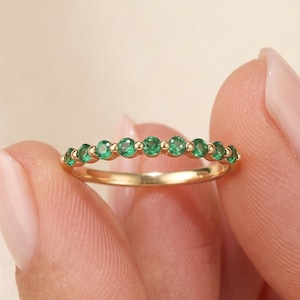 Könnte beinhalten: Ein Goldring mit einer Reihe von neun kleinen, runden, leuchtend grünen Edelsteinen, die entlang der oberen Hälfte der Ringschiene gefasst sind. Der Ring hat eine polierte Oberfläche und ein schmales, zierliches Profil.