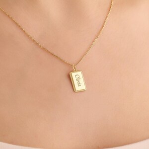 May include: A gold-toned necklace featuring a delicate chain and a rectangular pendant with a rope-style border. The pendant is engraved with the name Olivia in a clear, centred font, creating a simple and refined piece of jewellery.