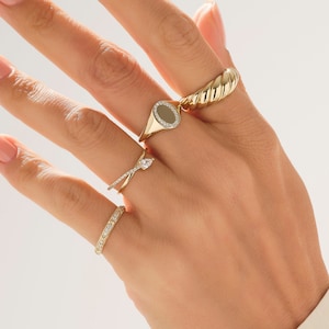 May include: A set of four gold rings with different designs. The rings are worn on a hand, with the largest ring on the index finger and the smallest ring on the pinky finger.