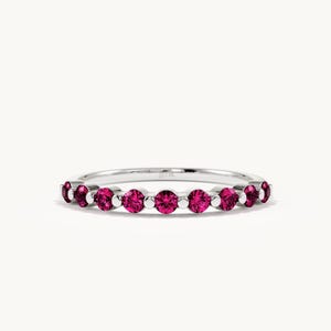 May include: A silver-toned ring featuring a series of round, vibrant pink gemstones set in a row. The band is thin and metallic, with small silver beads positioned between each of the circular pink stones, creating a continuous, symmetrical design.