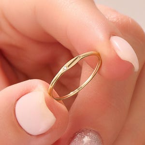 Peut inclure: Une fine bague en or avec une petite pierre précieuse transparente. La bague est tenue entre les doigts, mettant en valeur son design minimaliste et sa bande en or poli. La pierre précieuse est sertie dans un style simple et élégant. Le design de la bague est délicat et raffiné.