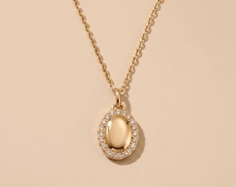 May include: A gold necklace featuring an oval-shaped pendant with a polished, smooth center. The pendant is framed by a border of small, clear, round-cut stones. The piece hangs from a delicate gold chain with a classic link design and a secure clasp.