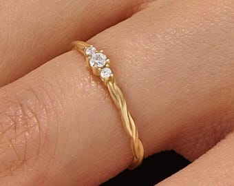 May include: A gold ring featuring a twisted band design with three small, clear, round-cut stones set in a row at the top. The metal has a polished finish, and the band exhibits a continuous spiral texture that wraps around the finger.