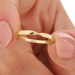 May include: A gold-colored ring with a twisted design. The ring is held between two fingers. The ring has the text "B14K" engraved on the inside. The ring is a simple band with a smooth, polished finish.