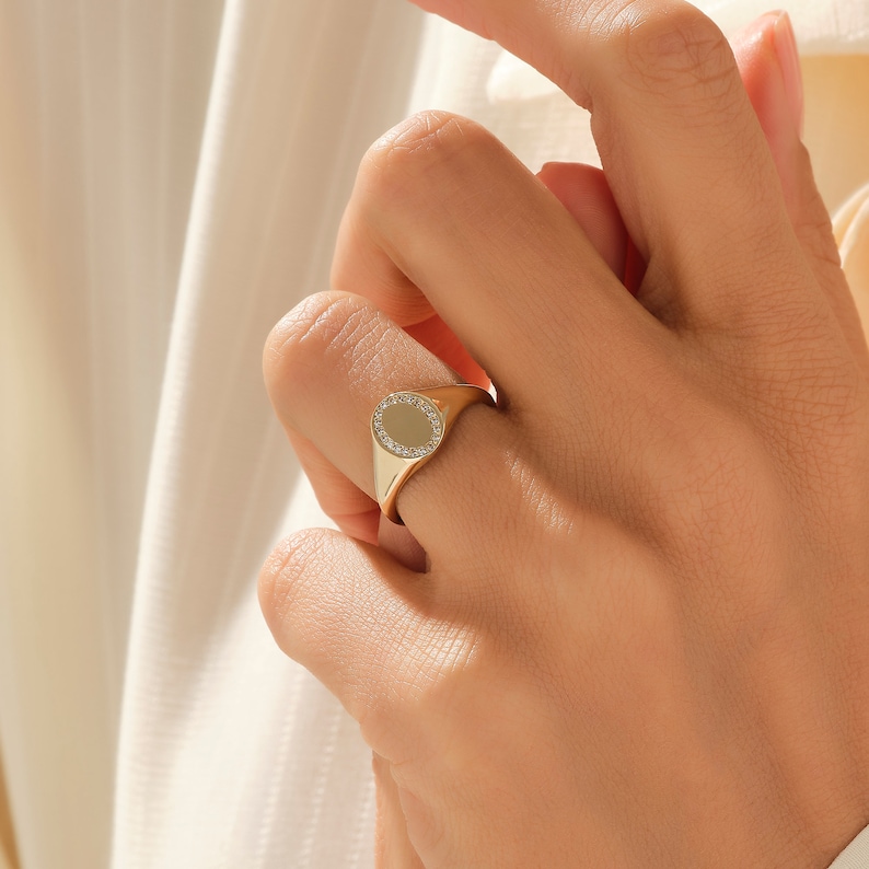 May include: A gold signet ring with a round, pave-set diamond center.