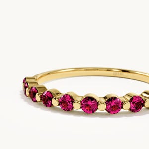 May include: A yellow gold band ring featuring a series of round, vibrant pink gemstones set in a row. The metal band is polished and smooth, with the engraving 14K visible on the inner surface of the ring, showcasing a classic design with stones.