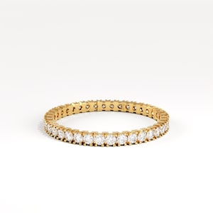 May include: A gold eternity ring with a continuous row of round, clear gemstones. The ring is set against a white background, highlighting the sparkle of the gemstones and the warm tone of the gold.