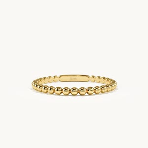 Op de afbeelding: Een geelgouden ring bestaande uit een doorlopende band van kleine, gepolijste bolvormige kralen. De ring heeft een glad, plat rechthoekig segment aan de bovenzijde, dat duidelijk is gegraveerd met de tekst 14K voor goudzuiverheid.
