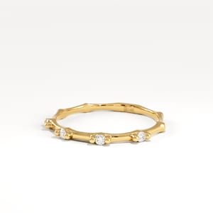 May include: A delicate gold ring with a branch-like design. The ring features several small, round, clear gemstones set along the band. The ring is set against a white background, highlighting its intricate details and elegant simplicity.