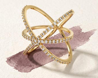 May include: A gold ring featuring a multi-layered, crisscross design with two intersecting bands. The surface of the bands is encrusted with small, clear, round-cut stones that catch the light, creating a continuous sparkling effect.