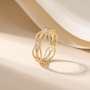 Op de afbeelding: Een goudkleurige ring met een ingewikkeld, verweven ontwerp. De ring is versierd met kleine, sprankelende edelstenen die in het verweven patroon zijn gezet. De ring wordt gepresenteerd tegen een neutrale achtergrond, waardoor de elegante details worden benadrukt.