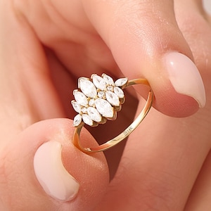 May include: A gold ring featuring a cluster of marquise-cut clear stones arranged in a fan-like pattern. The thin gold band is stamped with the text 14K on the inner surface, indicating the metal purity of the jewellery piece.