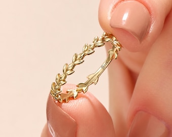 Könnte beinhalten: Ein dünner Goldring mit einem durchgehenden Band aus kleinen, zarten Blättern. Die Innenseite des Rings ist deutlich mit der Gravur 14K versehen, was den Goldgehalt angibt. Der Ring hat eine polierte Oberfläche und ein schmales Design.