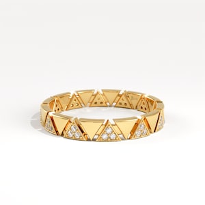 May include: A gold ring with a repeating pattern of triangular shapes. Some triangles are embellished with small, sparkling gemstones. The ring is set against a white background, emphasising its geometric design and luxurious appearance.
