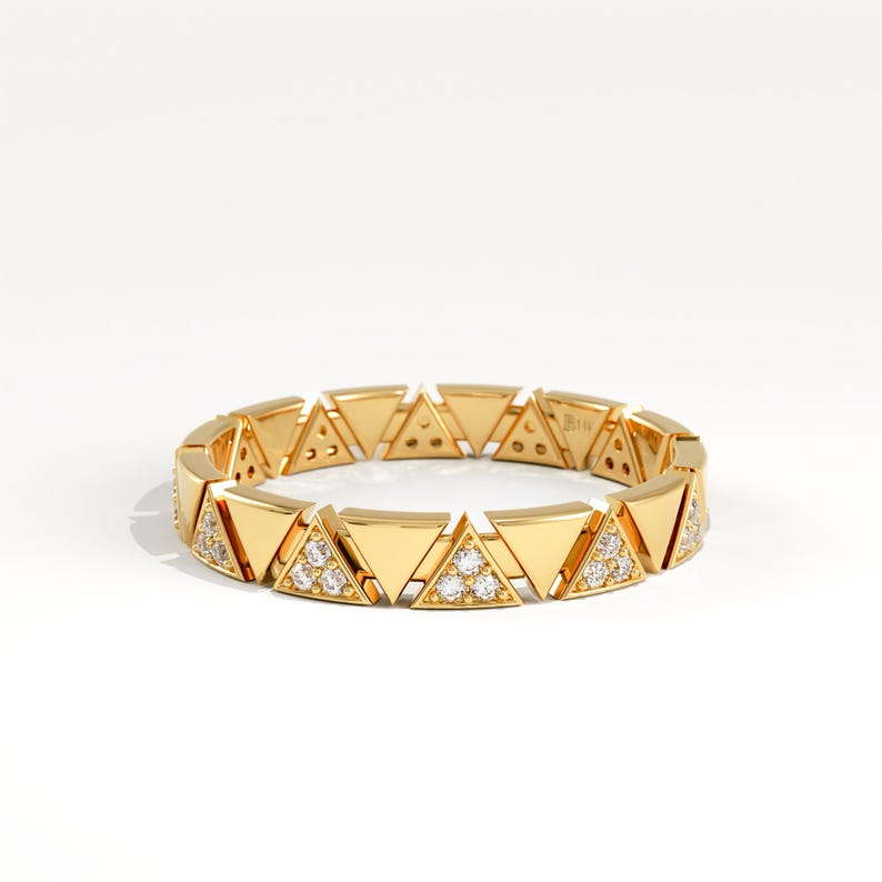 May include: A gold ring with a repeating pattern of triangular shapes. Some triangles are embellished with small, sparkling gemstones. The ring is set against a white background, emphasising its geometric design and luxurious appearance.