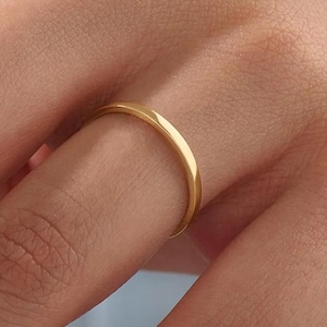 May include: A close-up of a gold ring. The ring is a thin band with a smooth, polished surface. The ring is worn on a finger, and the gold colour is bright and reflective.