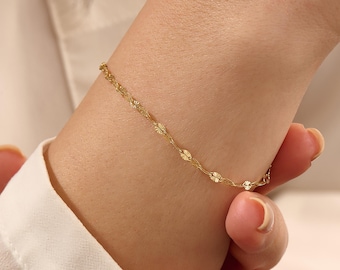 May include: A delicate gold chain bracelet featuring small, evenly spaced, circular textured links that catch the light. The bracelet is thin and minimalist in its construction, showcasing a polished finish that creates a subtle, shimmering effect.
