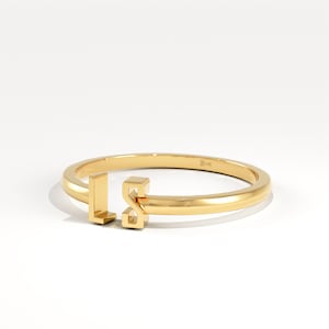 May include: A gold ring featuring the letters "LS" in a contemporary style. The ring is displayed on a white surface, emphasizing its shiny appearance. The design is minimalist, making it a versatile piece of jewellery for any occasion.