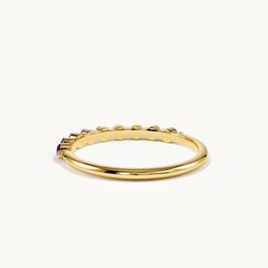 May include: A polished yellow gold ring featuring a series of small, round, deep red gemstones set along the top half of the band. The band has a smooth, rounded profile and a high-shine metallic finish, showcasing a minimalist and elegant design.