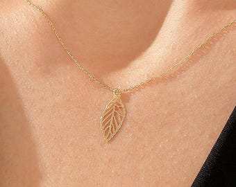 May include: A delicate gold-tone necklace featuring a small, openwork leaf pendant suspended from a fine chain. The pendant displays a detailed, skeletal leaf vein pattern, creating a lightweight and airy appearance against the skin.