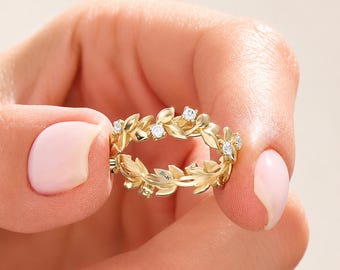 May include: A gold ring featuring a band designed with interconnected leaves and small, clear, round-cut stones set within the foliage. The interior of the band is clearly engraved with the text 14K.