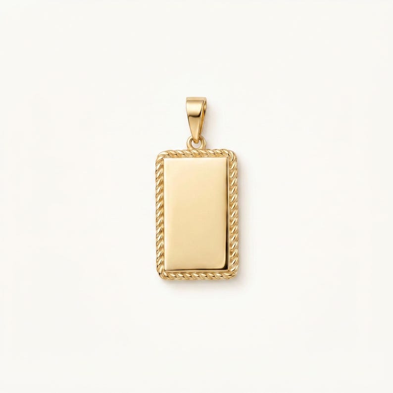May include: A rectangular gold pendant featuring a smooth, polished centre surface framed by a textured rope-style border. The pendant includes a small, triangular gold bail at the top for attachment to a chain, showcasing a clean, metallic finish.