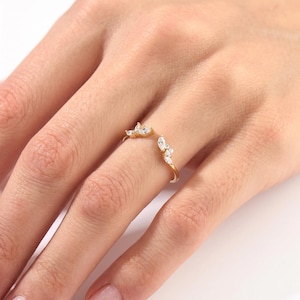 May include: A gold open-style ring featuring two clusters of marquise-cut clear stones at each end. The band is thin and polished, with the stones arranged in a leaf-like pattern on both sides of the opening, creating a delicate and symmetrical look.