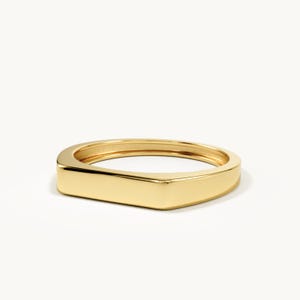 Peut inclure: Une bague en or poli dotée d'une surface supérieure plate et rectangulaire ainsi que d'un anneau lisse et continu. Le métal présente une finition brillante et réfléchissante, formant une silhouette géométrique simple et épurée.