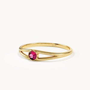 May include: A 14K gold ring featuring a split shank design and a single round, faceted, vibrant pink gemstone set in the center. The interior of the band is clearly stamped with the text 14K, indicating the gold purity of the metal.