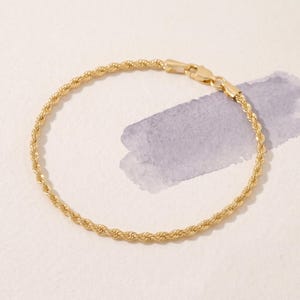 May include: A gold rope chain bracelet featuring a twisted metal design and a secure lobster claw clasp. The bracelet is formed into a circular shape, showcasing the uniform, spiraling texture of the gold links throughout the entire piece.