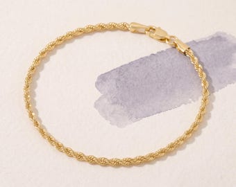 Könnte beinhalten: Ein goldenes Kordelkettenarmband mit gedrehtem Metalldesign und einem sicheren Karabinerverschluss. Das Armband ist kreisförmig geformt und zeigt die gleichmäßige, spiralförmige Textur der goldenen Glieder über das gesamte Schmuckstück hinweg.