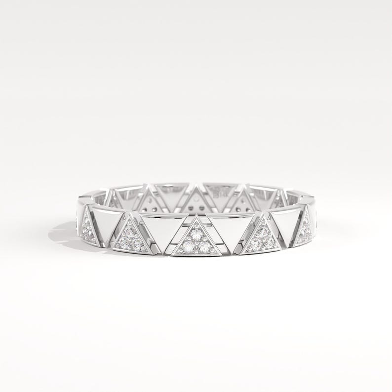 May include: A silver ring with a repeating triangular design. Each triangle alternates between a smooth, reflective surface and a section with small, sparkling gemstones. The ring is set against a white background.