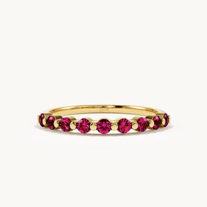 May include: A gold band ring featuring a row of seven round-cut vibrant pink gemstones. Each gemstone is set in a circular gold setting, alternating with small gold spheres along the band. The metal has a polished finish and a thin, delicate profile.