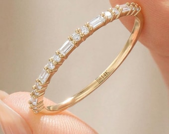 May include: A thin 14K gold ring featuring a delicate band set with alternating baguette-cut and round-cut clear stones. The interior of the band is clearly engraved with the text 14K, indicating the gold purity of the jewelry piece.