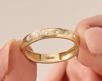May include: A gold band ring featuring six small, round, clear stones set flush into the top surface. The interior of the band is clearly stamped with the text B14K, indicating the metal purity of the gold ring in this jewelry piece.